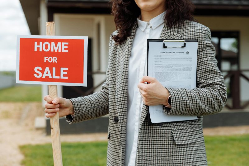 Home 3 A real estate agent holding a home for sale sign and clipboa 1779814844